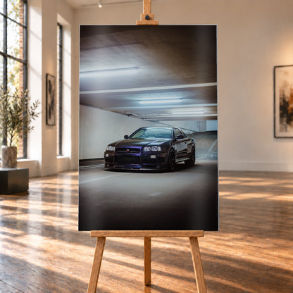 Dunkel lackierter Nissan Skyline R34 in frontaler Dreiviertelansicht in einer Betongarage mit weißen Deckenleuchten, Fahrbahnmarkierungen und ansteigender Rampe im Hintergrund; Visualisierung als Alu gebürstet-Wandbild, auf einer Holzstaffelei in einem hellen Galerieraum.