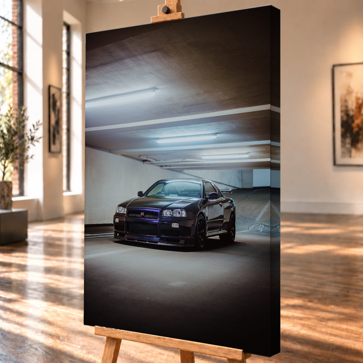 Dunkel lackierter Nissan Skyline R34 in frontaler Dreiviertelansicht in einer Betongarage mit weißen Deckenleuchten, Fahrbahnmarkierungen und ansteigender Rampe im Hintergrund; Visualisierung als Leinwand-Wandbild, schräg von der Seite auf einer Holzstaffelei.