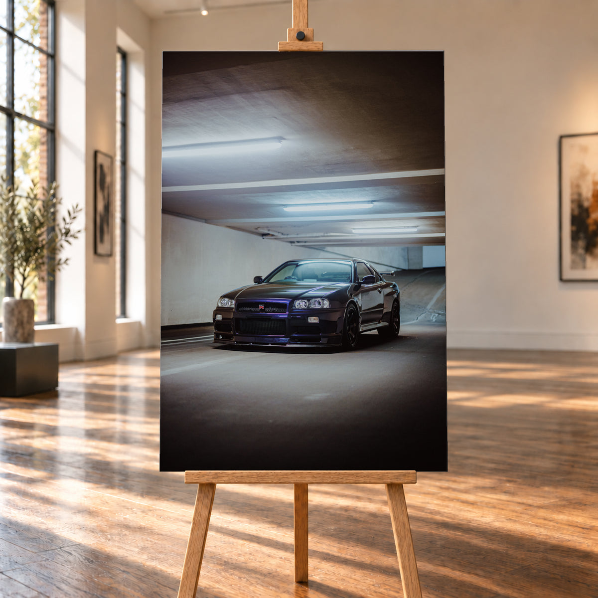 Dunkel lackierter Nissan Skyline R34 in frontaler Dreiviertelansicht in einer Betongarage mit weißen Deckenleuchten, Fahrbahnmarkierungen und ansteigender Rampe im Hintergrund; Visualisierung als Leinwand-Wandbild, auf einer Holzstaffelei in einem hellen Galerieraum.