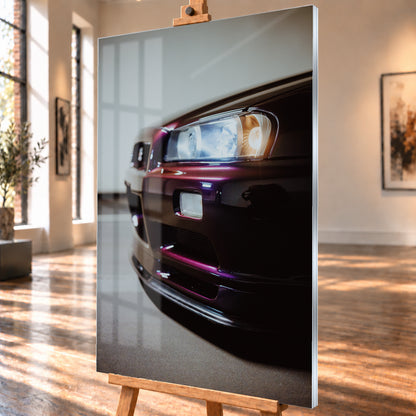 Nahaufnahme der Front eines dunklen, bordeauxviolett wirkenden Nissan Skyline V-Spec aus niedriger, schräger Perspektive. Ein rechteckiger Scheinwerfer mit kühlen und warmen Lichtanteilen dominiert die rechte Bildhälfte. Darunter sind Frontschürze, Leuchte und Lufteinlass zu sehen; eine hellgraue Wand und ein grauer Boden bilden den unscharfen Hintergrund; Visualisierung als Acrylglas-Wandbild, schräg von der Seite auf einer Holzstaffelei.