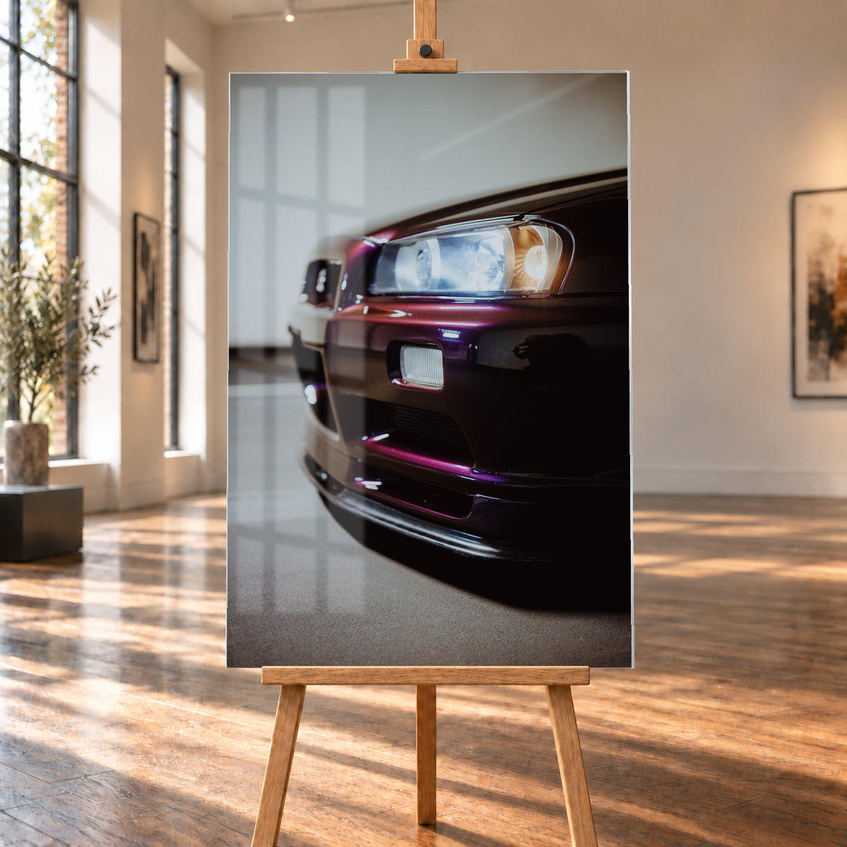 Nahaufnahme der Front eines dunklen, bordeauxviolett wirkenden Nissan Skyline V-Spec aus niedriger, schräger Perspektive. Ein rechteckiger Scheinwerfer mit kühlen und warmen Lichtanteilen dominiert die rechte Bildhälfte. Darunter sind Frontschürze, Leuchte und Lufteinlass zu sehen; eine hellgraue Wand und ein grauer Boden bilden den unscharfen Hintergrund; Visualisierung als Acrylglas-Wandbild, auf einer Holzstaffelei in einem hellen Galerieraum.