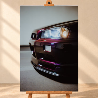 Nahaufnahme der Front eines dunklen, bordeauxviolett wirkenden Nissan Skyline V-Spec aus niedriger, schräger Perspektive. Ein rechteckiger Scheinwerfer mit kühlen und warmen Lichtanteilen dominiert die rechte Bildhälfte. Darunter sind Frontschürze, Leuchte und Lufteinlass zu sehen; eine hellgraue Wand und ein grauer Boden bilden den unscharfen Hintergrund; Visualisierung als Leinwand-Wandbild, frontal auf einer Holzstaffelei.