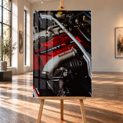 Nahaufnahme eines Motorraums mit roter Abdeckung und sichtbarem SKYLINE GT-R-Schriftzug, hellem Rohr mit TWIN TURBO-Kennzeichnung, schwarzer Verrohrung und einer silbernen, diagonal verlaufenden Strebe; dunkler Hintergrund mit warmen Lichtreflexen; Visualisierung als Acrylglas-Wandbild, auf einer Holzstaffelei in einem hellen Galerieraum.