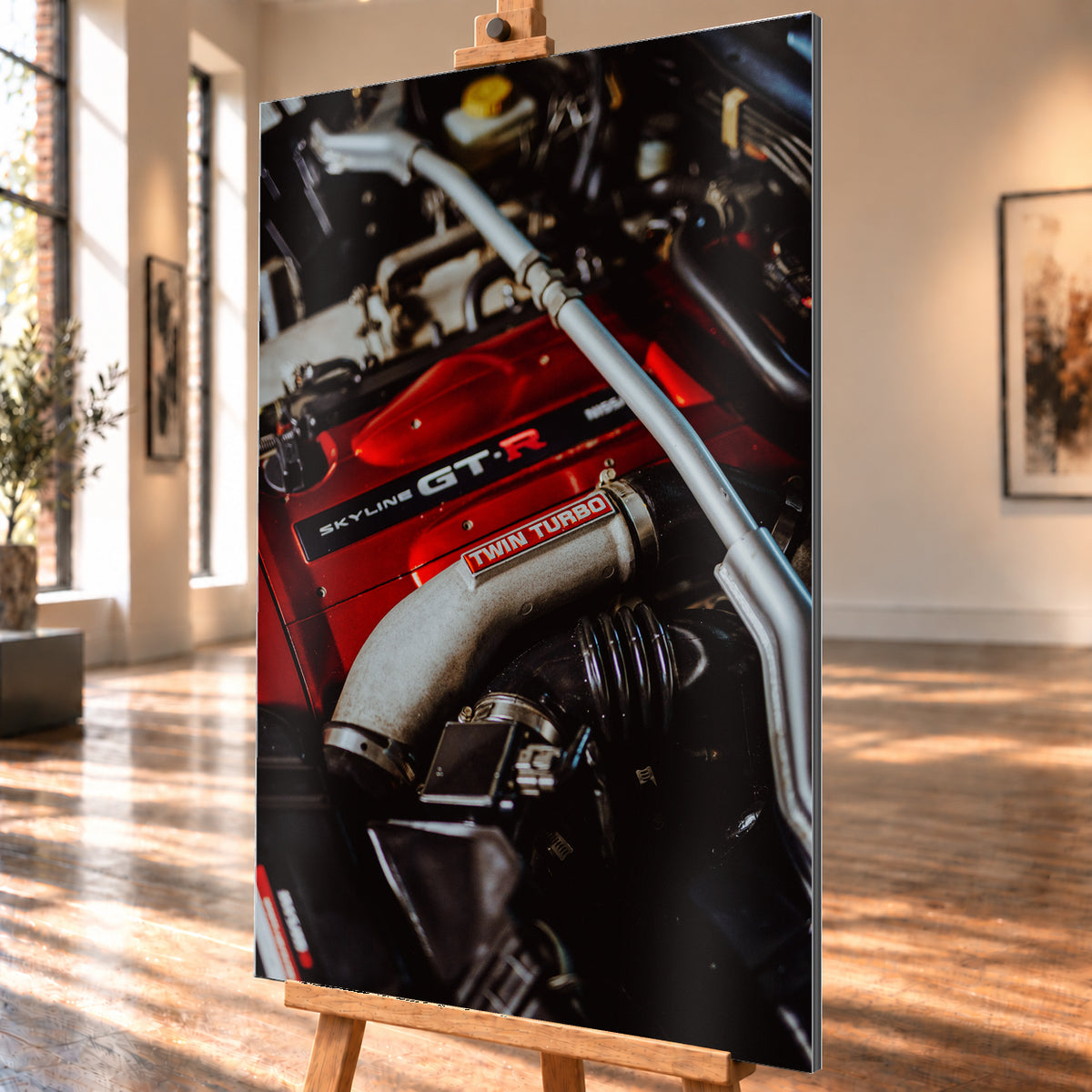 Nahaufnahme eines Motorraums mit roter Abdeckung und sichtbarem SKYLINE GT-R-Schriftzug, hellem Rohr mit TWIN TURBO-Kennzeichnung, schwarzer Verrohrung und einer silbernen, diagonal verlaufenden Strebe; dunkler Hintergrund mit warmen Lichtreflexen; Visualisierung als Alu gebürstet-Wandbild, schräg von der Seite auf einer Holzstaffelei.