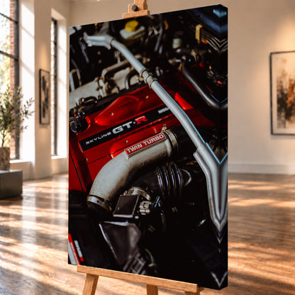 Nahaufnahme eines Motorraums mit roter Abdeckung und sichtbarem SKYLINE GT-R-Schriftzug, hellem Rohr mit TWIN TURBO-Kennzeichnung, schwarzer Verrohrung und einer silbernen, diagonal verlaufenden Strebe; dunkler Hintergrund mit warmen Lichtreflexen; Visualisierung als Leinwand-Wandbild, schräg von der Seite auf einer Holzstaffelei.