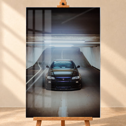 Dunkler Nissan Skyline R34 GT-R in frontaler, mittiger Ansicht auf einer ansteigenden Parkhausrampe unter hellen Deckenleuchten; weiße Fahrbahnmarkierungen, Betonwände und kühl blau-violette Reflexe prägen die Szene; Visualisierung als Acrylglas-Wandbild, frontal auf einer Holzstaffelei.
