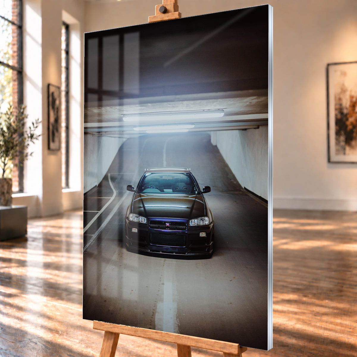 Dunkler Nissan Skyline R34 GT-R in frontaler, mittiger Ansicht auf einer ansteigenden Parkhausrampe unter hellen Deckenleuchten; weiße Fahrbahnmarkierungen, Betonwände und kühl blau-violette Reflexe prägen die Szene; Visualisierung als Acrylglas-Wandbild, schräg von der Seite auf einer Holzstaffelei.