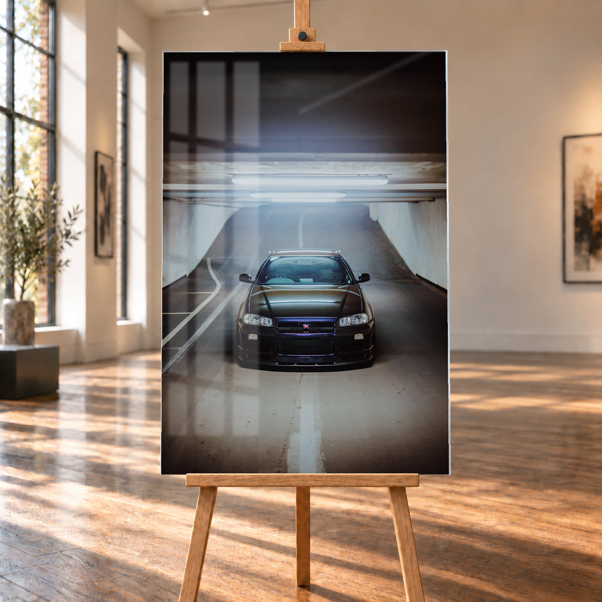 Dunkler Nissan Skyline R34 GT-R in frontaler, mittiger Ansicht auf einer ansteigenden Parkhausrampe unter hellen Deckenleuchten; weiße Fahrbahnmarkierungen, Betonwände und kühl blau-violette Reflexe prägen die Szene; Visualisierung als Acrylglas-Wandbild, auf einer Holzstaffelei in einem hellen Galerieraum.