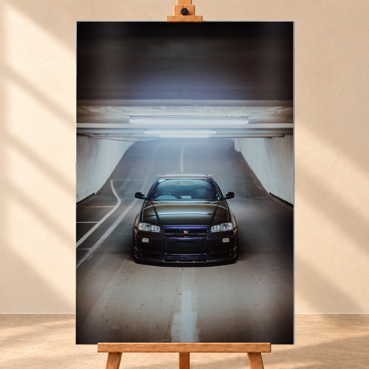 Dunkler Nissan Skyline R34 GT-R in frontaler, mittiger Ansicht auf einer ansteigenden Parkhausrampe unter hellen Deckenleuchten; weiße Fahrbahnmarkierungen, Betonwände und kühl blau-violette Reflexe prägen die Szene; Visualisierung als Alu gebürstet-Wandbild, frontal auf einer Holzstaffelei.