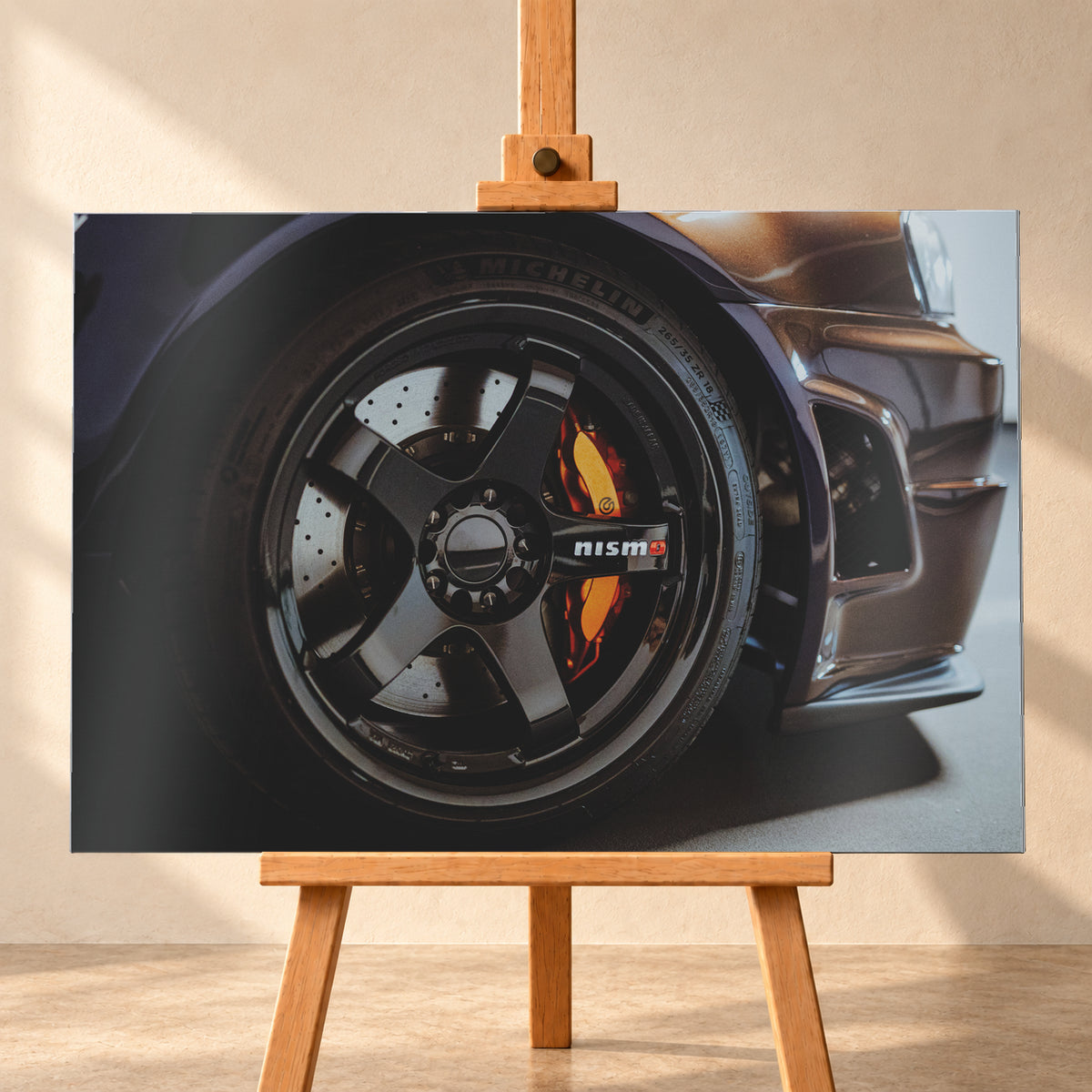 Nahaufnahme der Frontpartie eines dunkelviolett-bronze schimmernden Nissan Skyline R34 mit schwarzem Rad, sichtbarem NISMO-Schriftzug, gelochter Bremsscheibe und orange-rotem Bremssattel bei kontrastreichem Licht; Visualisierung als Alu gebürstet-Wandbild, frontal auf einer Holzstaffelei.