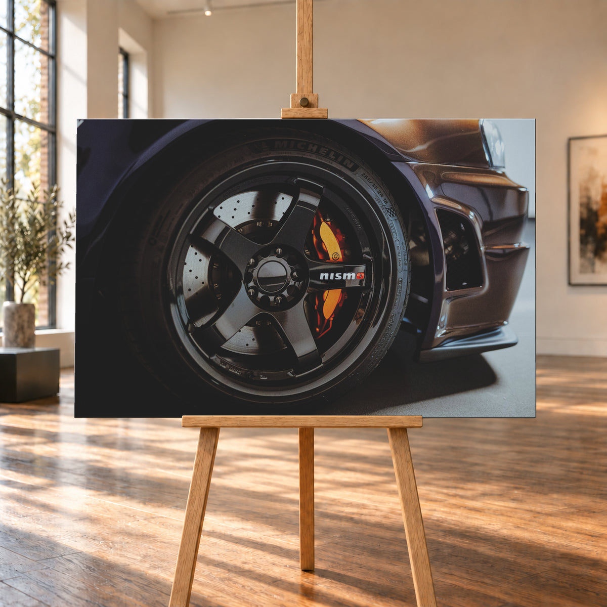Nahaufnahme der Frontpartie eines dunkelviolett-bronze schimmernden Nissan Skyline R34 mit schwarzem Rad, sichtbarem NISMO-Schriftzug, gelochter Bremsscheibe und orange-rotem Bremssattel bei kontrastreichem Licht; Visualisierung als Leinwand-Wandbild, auf einer Holzstaffelei in einem hellen Galerieraum.
