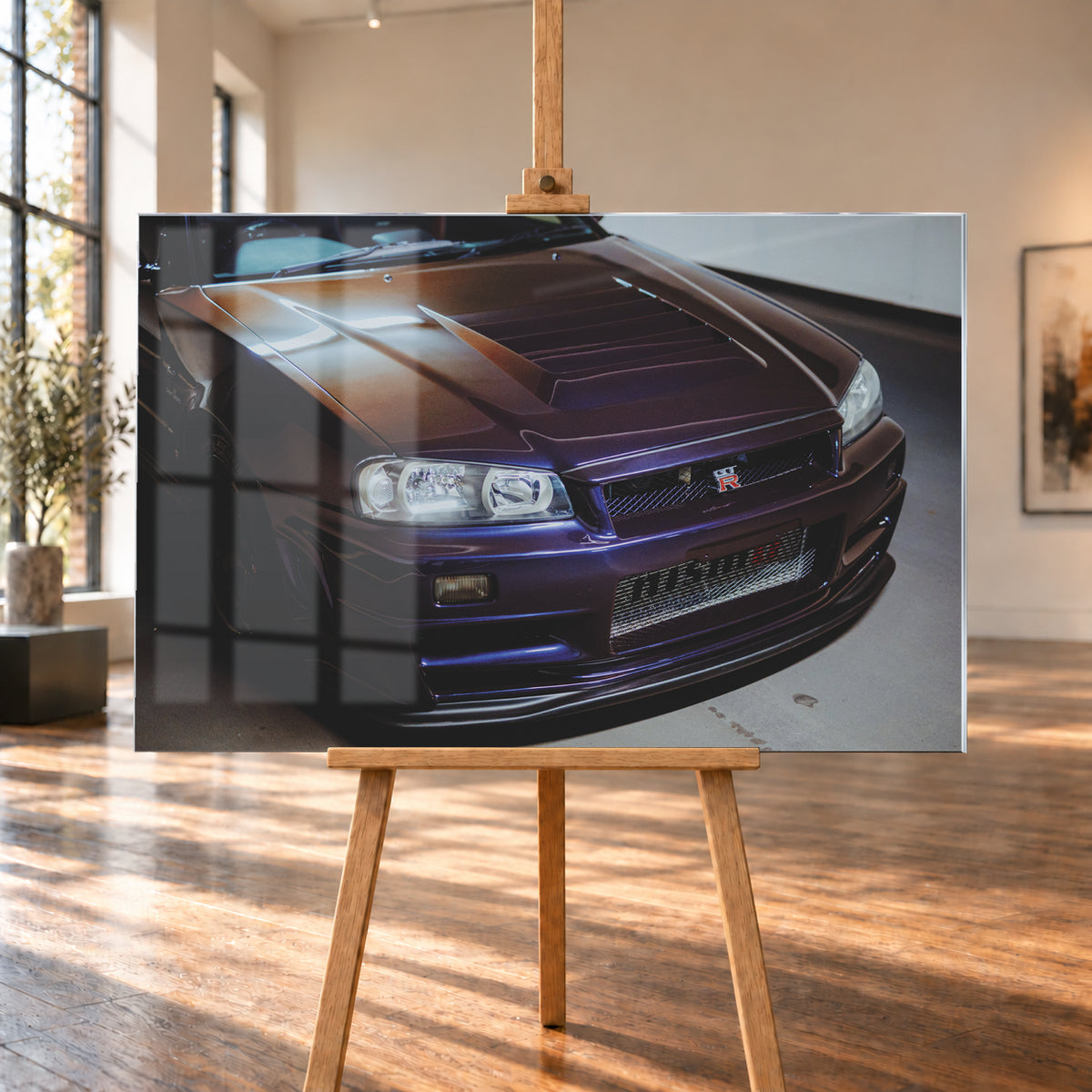 Nahes Frontporträt eines Nissan Skyline R34 in violett schimmerndem Lack, leicht von oben fotografiert, mit konturierter Motorhaube, Scheinwerfern, Kühlergrill und breiten Lufteinlässen in einem hellen Innenraum; Visualisierung als Acrylglas-Wandbild, auf einer Holzstaffelei in einem hellen Galerieraum.