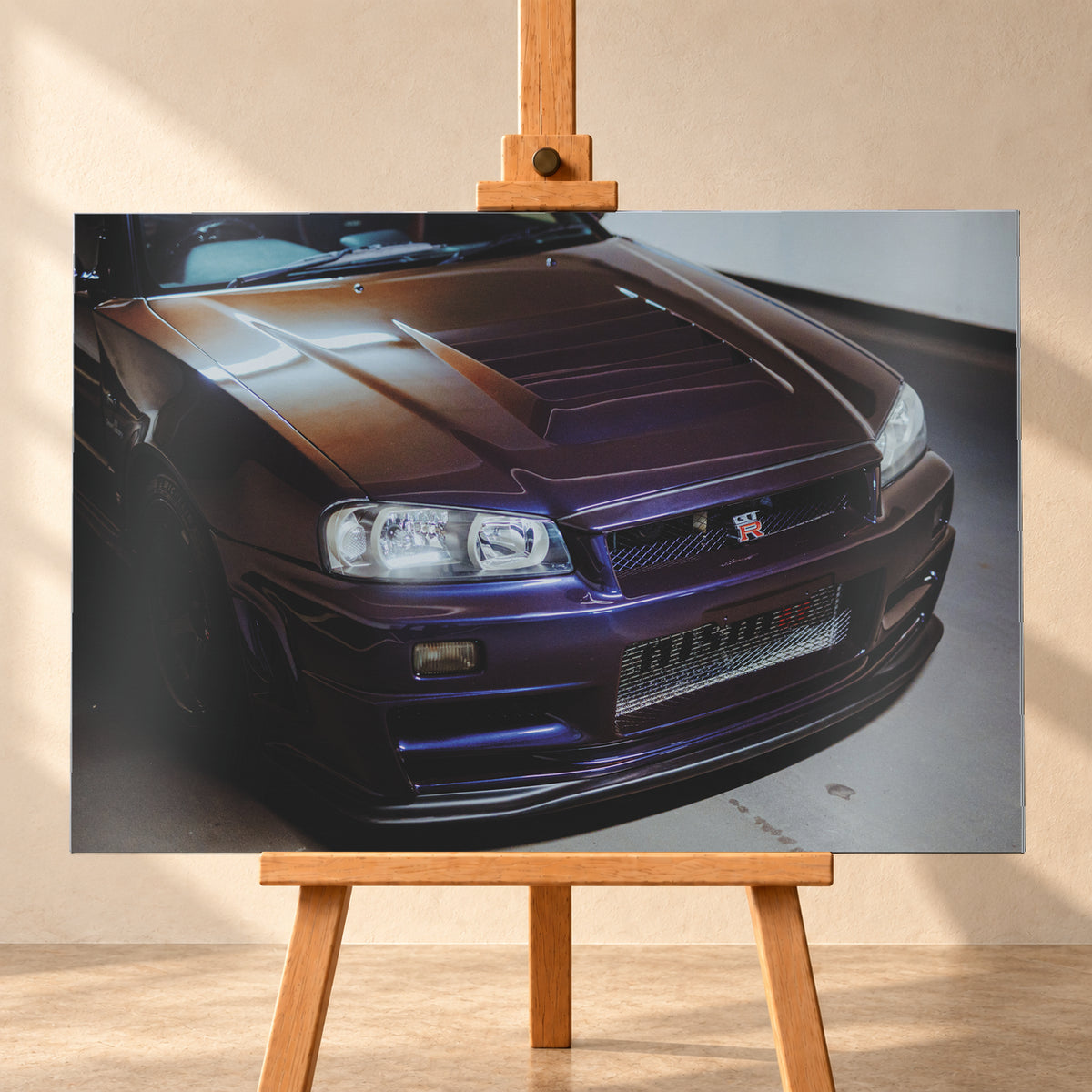 Nahes Frontporträt eines Nissan Skyline R34 in violett schimmerndem Lack, leicht von oben fotografiert, mit konturierter Motorhaube, Scheinwerfern, Kühlergrill und breiten Lufteinlässen in einem hellen Innenraum; Visualisierung als Alu gebürstet-Wandbild, frontal auf einer Holzstaffelei.