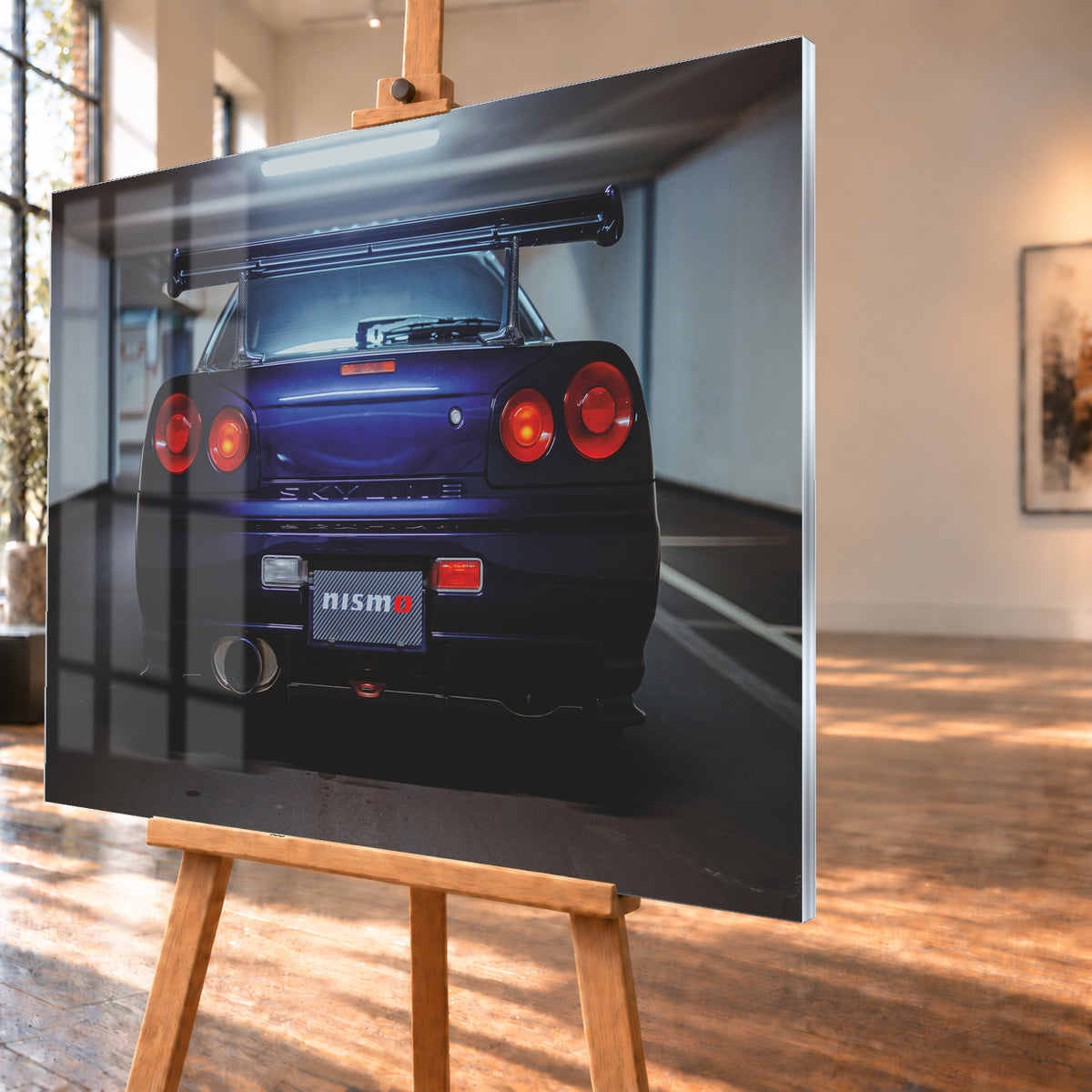 Zentrierte Heckansicht eines dunkelvioletten Nissan Skyline R34 in einer Parkgarage. Sichtbar sind vier runde rote Rückleuchten mit orangefarbenen inneren Leuchtelementen, ein großer Heckflügel, ein breites Auspuffendrohr links, ein Nismo-Schriftzug und kühles Deckenlicht über dem Fahrzeug; Visualisierung als Acrylglas-Wandbild, schräg von der Seite auf einer Holzstaffelei.