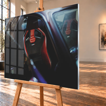 Seitlicher Nahblick in den dunklen Innenraum eines Nissan Skyline R34. Ein rot-schwarzer Sportsitz mit Öffnungen in der Rückenlehne und Nismo-Schriftzug steht im Zentrum; ein zweiter Sitz ist gegenüber sichtbar. Blau-violette Reflexe, Glasflächen und tiefe Schatten rahmen die Szene; Visualisierung als Acrylglas-Wandbild, schräg von der Seite auf einer Holzstaffelei.