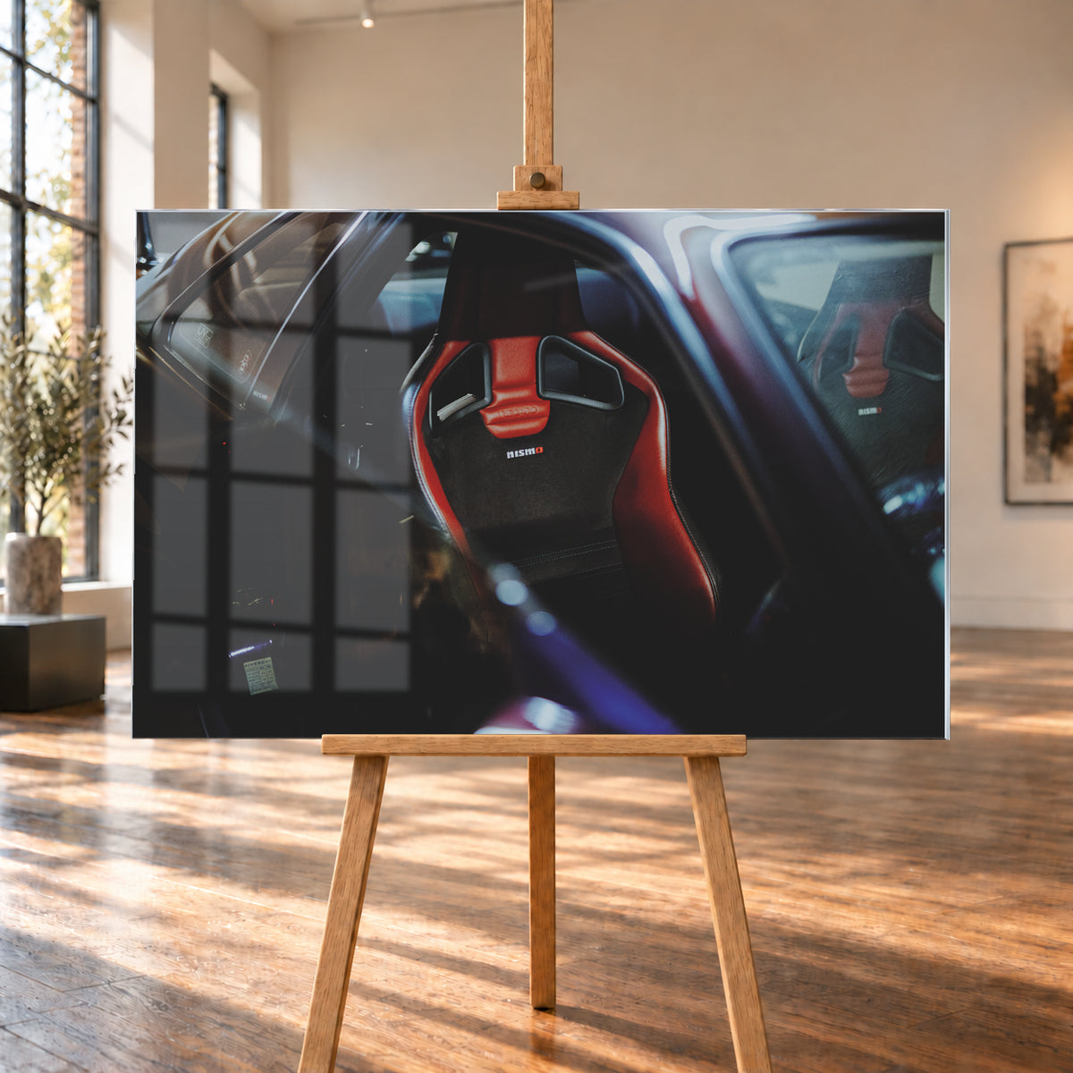 Seitlicher Nahblick in den dunklen Innenraum eines Nissan Skyline R34. Ein rot-schwarzer Sportsitz mit Öffnungen in der Rückenlehne und Nismo-Schriftzug steht im Zentrum; ein zweiter Sitz ist gegenüber sichtbar. Blau-violette Reflexe, Glasflächen und tiefe Schatten rahmen die Szene; Visualisierung als Acrylglas-Wandbild, auf einer Holzstaffelei in einem hellen Galerieraum.