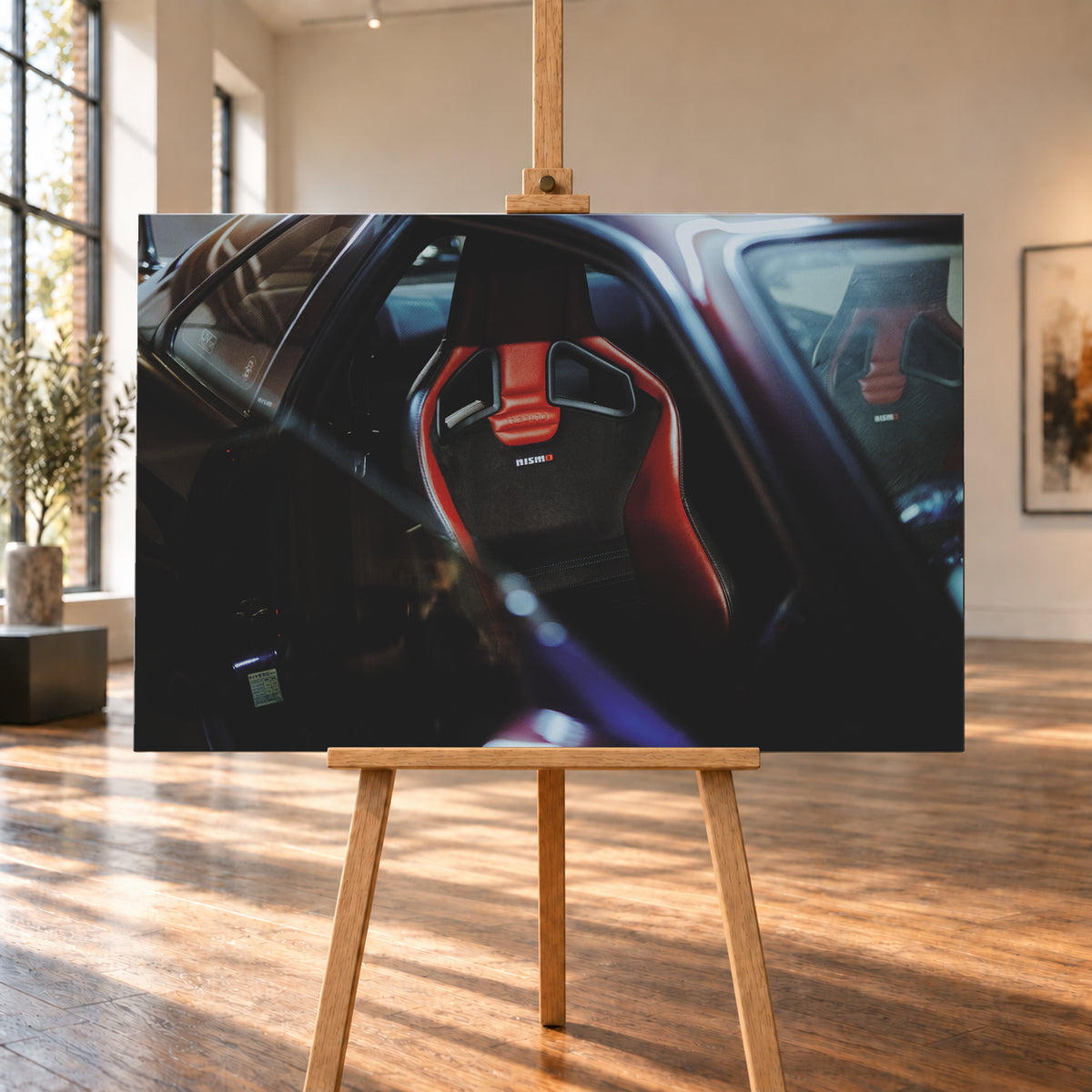 Seitlicher Nahblick in den dunklen Innenraum eines Nissan Skyline R34. Ein rot-schwarzer Sportsitz mit Öffnungen in der Rückenlehne und Nismo-Schriftzug steht im Zentrum; ein zweiter Sitz ist gegenüber sichtbar. Blau-violette Reflexe, Glasflächen und tiefe Schatten rahmen die Szene; Visualisierung als Leinwand-Wandbild, auf einer Holzstaffelei in einem hellen Galerieraum.