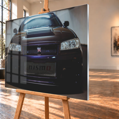 Symmetrische frontale Nahaufnahme eines dunkelvioletten Nissan Skyline R34 vor hellen Wänden. Sichtbar sind rechteckige Scheinwerfer, GT-R-Emblem, Hauben-Lufteinlass, Kühlergitter und die große untere Gitteröffnung; kühles Licht spiegelt sich auf Haube und Windschutzscheibe; Visualisierung als Acrylglas-Wandbild, schräg von der Seite auf einer Holzstaffelei.