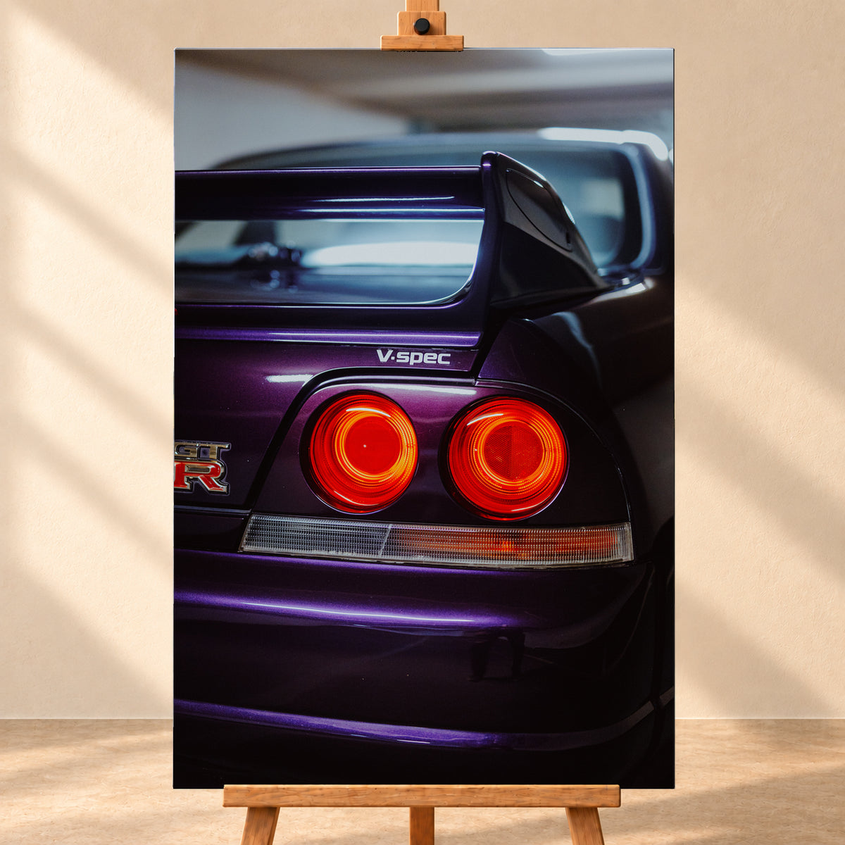 Vertikale Nahaufnahme des dunkelvioletten Hecks eines Nissan Skyline V-Spec mit zwei rot leuchtenden Rundrückleuchten, GT-R-Emblem, großem Heckflügel und blau-violetten Lichtreflexen vor unscharfem dunklem Hintergrund; Visualisierung als Leinwand-Wandbild, frontal auf einer Holzstaffelei.