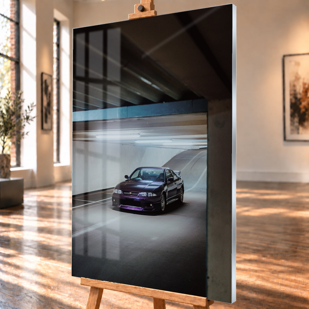 Dunkelvioletter Nissan Skyline in vorderer Dreiviertelansicht in einer Beton-Tiefgarage, beleuchtet von kühlen Deckenleuchten; Fahrbahnlinien und eine Rampe liegen im Hintergrund; Visualisierung als Acrylglas-Wandbild, schräg von der Seite auf einer Holzstaffelei.
