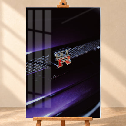 Nahaufnahme eines rot-silbernen GT-R-Emblems an einem dunklen Frontgrill, beleuchtet von violettem Licht und umgeben von tiefen Schatten; Visualisierung als Acrylglas-Wandbild, frontal auf einer Holzstaffelei.