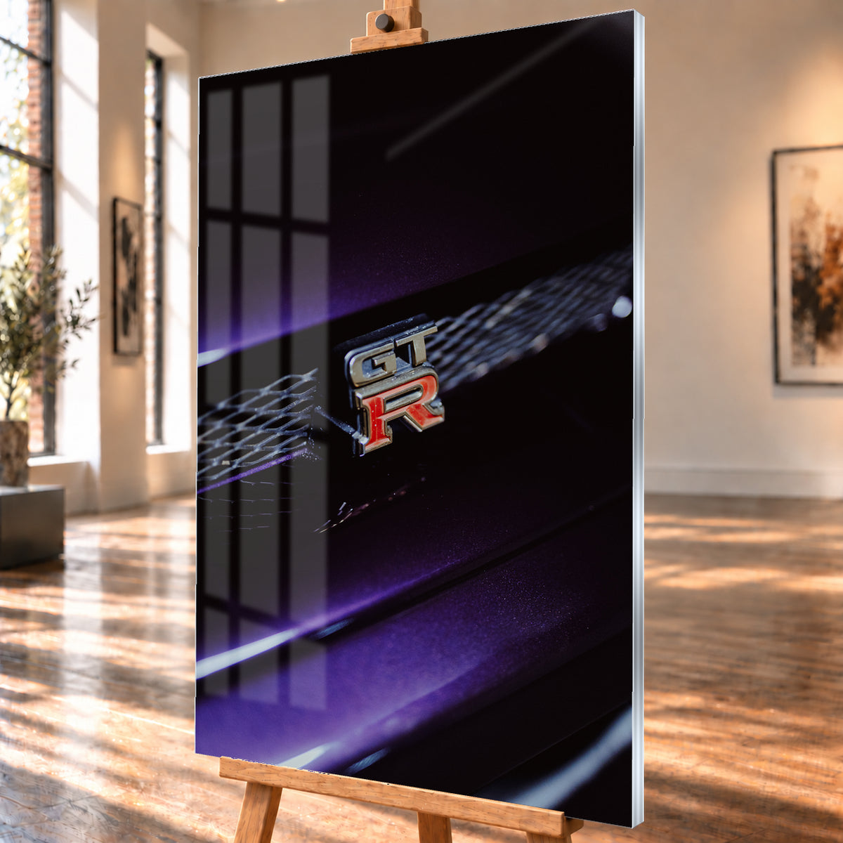 Nahaufnahme eines rot-silbernen GT-R-Emblems an einem dunklen Frontgrill, beleuchtet von violettem Licht und umgeben von tiefen Schatten; Visualisierung als Acrylglas-Wandbild, schräg von der Seite auf einer Holzstaffelei.