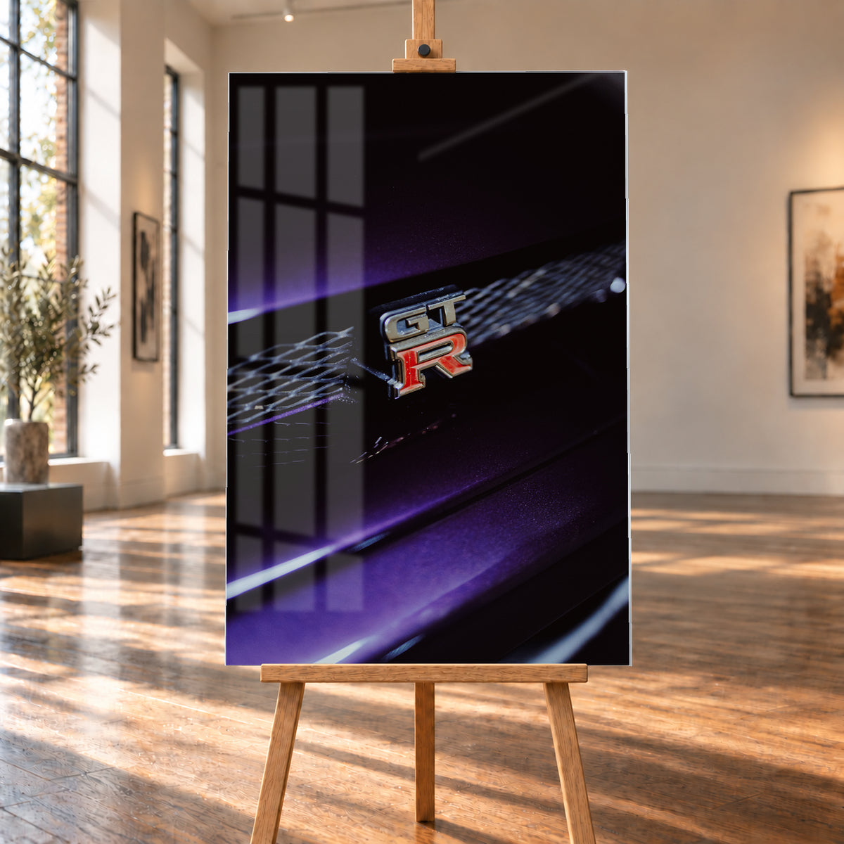 Nahaufnahme eines rot-silbernen GT-R-Emblems an einem dunklen Frontgrill, beleuchtet von violettem Licht und umgeben von tiefen Schatten; Visualisierung als Acrylglas-Wandbild, auf einer Holzstaffelei in einem hellen Galerieraum.