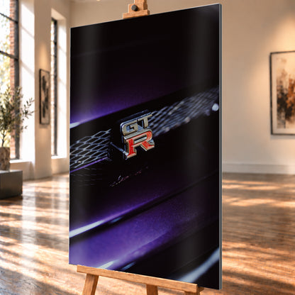Nahaufnahme eines rot-silbernen GT-R-Emblems an einem dunklen Frontgrill, beleuchtet von violettem Licht und umgeben von tiefen Schatten; Visualisierung als Alu gebürstet-Wandbild, schräg von der Seite auf einer Holzstaffelei.