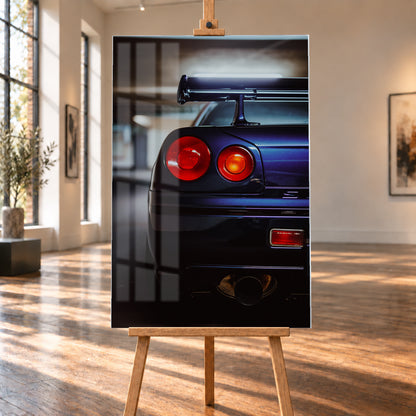 Hochformatige Nahaufnahme des Hecks eines dunkelblau-violetten Nissan Skyline V-Spec von 1999 in einem unscharfen, garagenartigen Innenraum; sichtbar sind zwei runde rote Rückleuchten, ein großer Heckflügel und ein rundes Auspuffendrohr am unteren Bildrand; Visualisierung als Acrylglas-Wandbild, auf einer Holzstaffelei in einem hellen Galerieraum.