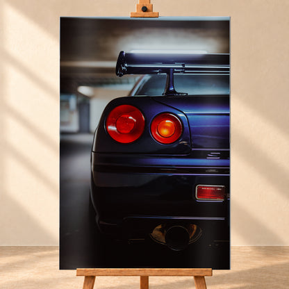 Hochformatige Nahaufnahme des Hecks eines dunkelblau-violetten Nissan Skyline V-Spec von 1999 in einem unscharfen, garagenartigen Innenraum; sichtbar sind zwei runde rote Rückleuchten, ein großer Heckflügel und ein rundes Auspuffendrohr am unteren Bildrand; Visualisierung als Alu gebürstet-Wandbild, frontal auf einer Holzstaffelei.