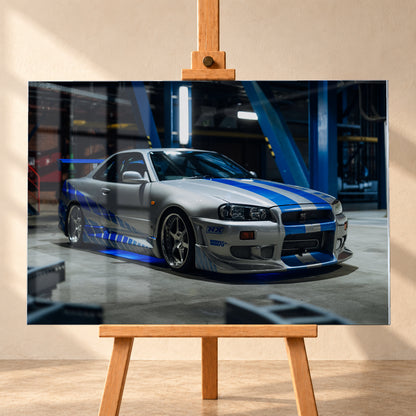 Silberner Nissan Skyline GT-R R34 mit blauen Streifen und Seitengrafik in tiefer Front-Dreiviertelansicht. Das Fahrzeug steht auf Beton in einer dunklen Industriehalle mit blauen Stahlträgern, hellen Leuchten und blauem Licht unter der Karosserie. Frontschürze und großer Heckflügel sind sichtbar; Visualisierung als Acrylglas-Wandbild, frontal auf einer Holzstaffelei.