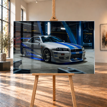 Silberner Nissan Skyline GT-R R34 mit blauen Streifen und Seitengrafik in tiefer Front-Dreiviertelansicht. Das Fahrzeug steht auf Beton in einer dunklen Industriehalle mit blauen Stahlträgern, hellen Leuchten und blauem Licht unter der Karosserie. Frontschürze und großer Heckflügel sind sichtbar; Visualisierung als Acrylglas-Wandbild, auf einer Holzstaffelei in einem hellen Galerieraum.