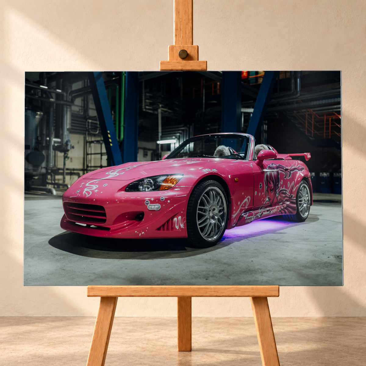 Pinker Honda S2000 als offener Roadster in Front-Dreiviertelansicht auf einem Betonboden in einer dunklen Industriehalle; sichtbar sind weiße Dekorgrafiken, eine große Frauenfigur an der Seite, silberne Mehrspeichenräder, ein Heckflügel und violett-blaues Licht unter dem Fahrzeug; Visualisierung als Alu gebürstet-Wandbild, frontal auf einer Holzstaffelei.
