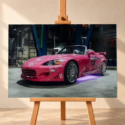 Pinker Honda S2000 als offener Roadster in Front-Dreiviertelansicht auf einem Betonboden in einer dunklen Industriehalle; sichtbar sind weiße Dekorgrafiken, eine große Frauenfigur an der Seite, silberne Mehrspeichenräder, ein Heckflügel und violett-blaues Licht unter dem Fahrzeug; Visualisierung als Alu gebürstet-Wandbild, frontal auf einer Holzstaffelei.