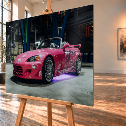 Pinker Honda S2000 als offener Roadster in Front-Dreiviertelansicht auf einem Betonboden in einer dunklen Industriehalle; sichtbar sind weiße Dekorgrafiken, eine große Frauenfigur an der Seite, silberne Mehrspeichenräder, ein Heckflügel und violett-blaues Licht unter dem Fahrzeug; Visualisierung als Alu gebürstet-Wandbild, schräg von der Seite auf einer Holzstaffelei.