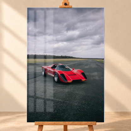 Roter Coyote X in Front-Dreiviertelansicht auf einer breiten dunklen Asphaltbahn. Das hochformatige Bild zeigt flache Wiesen, einen niedrigen Baumhorizont und einen ausgedehnten grauen Wolkenhimmel; Personen sind nicht sichtbar; Visualisierung als Acrylglas-Wandbild, frontal auf einer Holzstaffelei.