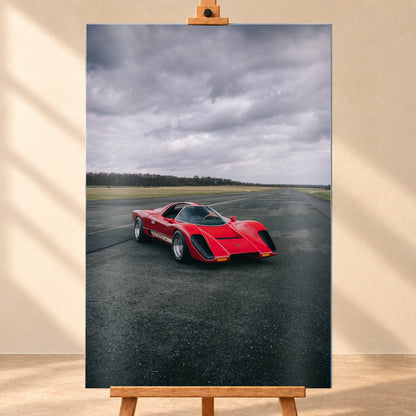 Roter Coyote X in Front-Dreiviertelansicht auf einer breiten dunklen Asphaltbahn. Das hochformatige Bild zeigt flache Wiesen, einen niedrigen Baumhorizont und einen ausgedehnten grauen Wolkenhimmel; Personen sind nicht sichtbar; Visualisierung als Alu gebürstet-Wandbild, frontal auf einer Holzstaffelei.