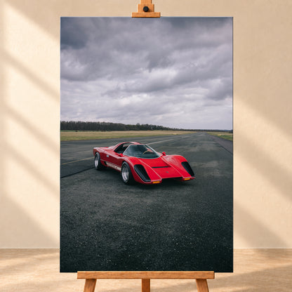 Roter Coyote X in Front-Dreiviertelansicht auf einer breiten dunklen Asphaltbahn. Das hochformatige Bild zeigt flache Wiesen, einen niedrigen Baumhorizont und einen ausgedehnten grauen Wolkenhimmel; Personen sind nicht sichtbar; Visualisierung als Leinwand-Wandbild, frontal auf einer Holzstaffelei.