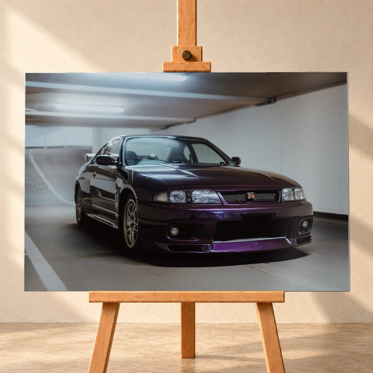 Der Nissan Skyline R33 steht tief in einer Dreiviertel-Frontansicht zwischen weißen Fahrbahnmarkierungen und kühlen Betonflächen. Motiv „Midnight Moment 2“ als Alu gebürstet-Wandbild, frontal auf einer Holzstaffelei.