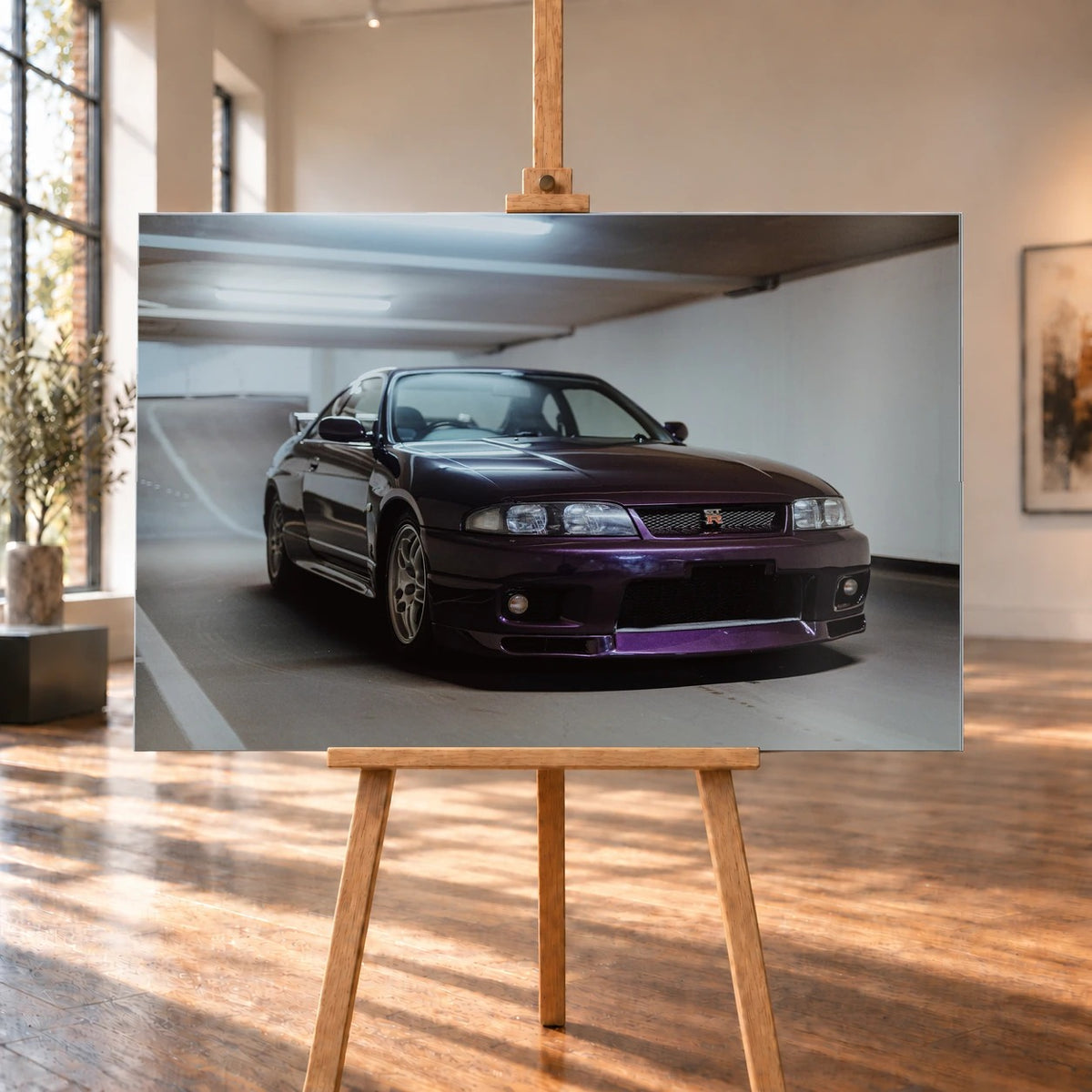 Der Nissan Skyline R33 steht tief in einer Dreiviertel-Frontansicht zwischen weißen Fahrbahnmarkierungen und kühlen Betonflächen. Motiv „Midnight Moment 2“ als Alu gebürstet-Wandbild, auf einer Holzstaffelei in einem hellen Galerieraum.