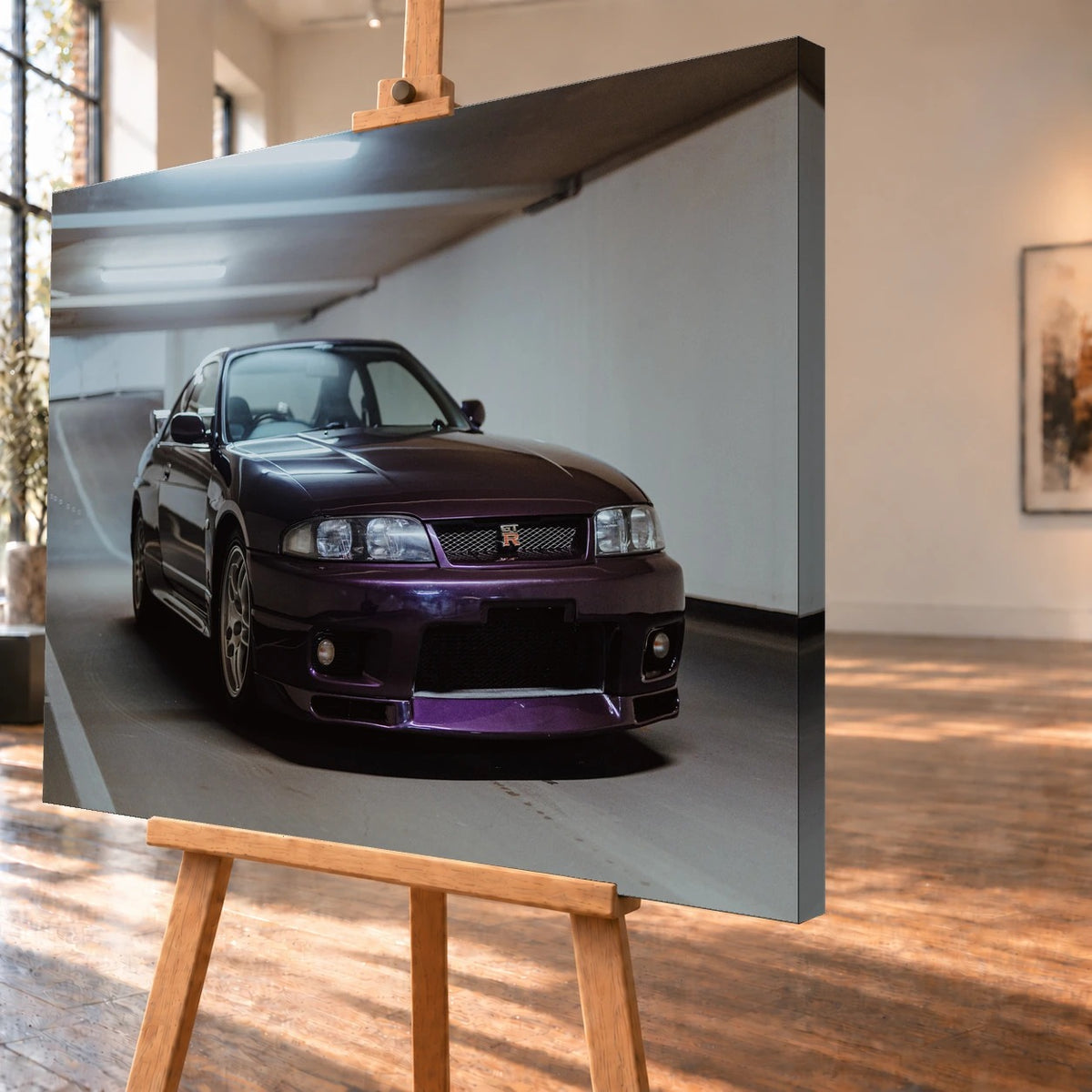 Der Nissan Skyline R33 steht tief in einer Dreiviertel-Frontansicht zwischen weißen Fahrbahnmarkierungen und kühlen Betonflächen. Motiv „Midnight Moment 2“ als Leinwand-Wandbild, schräg von der Seite auf einer Holzstaffelei.