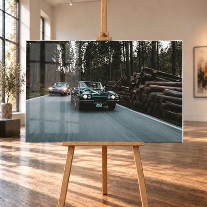 Eine grüne Corvette C2 und ein Porsche 911 S Softwindow fahren hintereinander durch einen Wald; Bewegungsunschärfe vermittelt Tempo. Motiv „Golden Light“ als Acrylglas-Wandbild, auf einer Holzstaffelei in einem hellen Galerieraum.