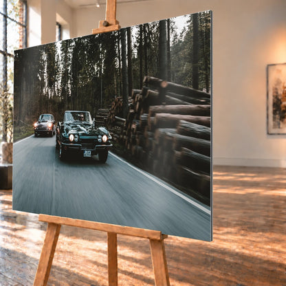 Eine grüne Corvette C2 und ein Porsche 911 S Softwindow fahren hintereinander durch einen Wald; Bewegungsunschärfe vermittelt Tempo. Motiv „Golden Light“ als Alu gebürstet-Wandbild, schräg von der Seite auf einer Holzstaffelei.