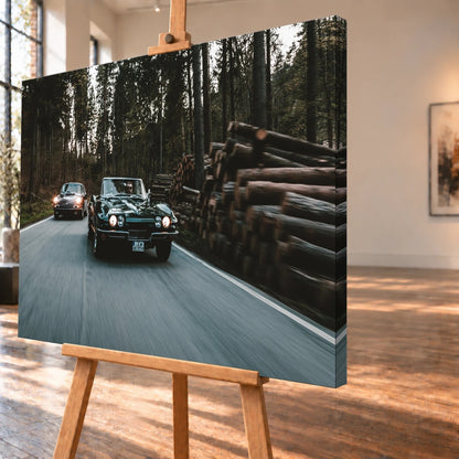Eine grüne Corvette C2 und ein Porsche 911 S Softwindow fahren hintereinander durch einen Wald; Bewegungsunschärfe vermittelt Tempo. Motiv „Golden Light“ als Leinwand-Wandbild, schräg von der Seite auf einer Holzstaffelei.