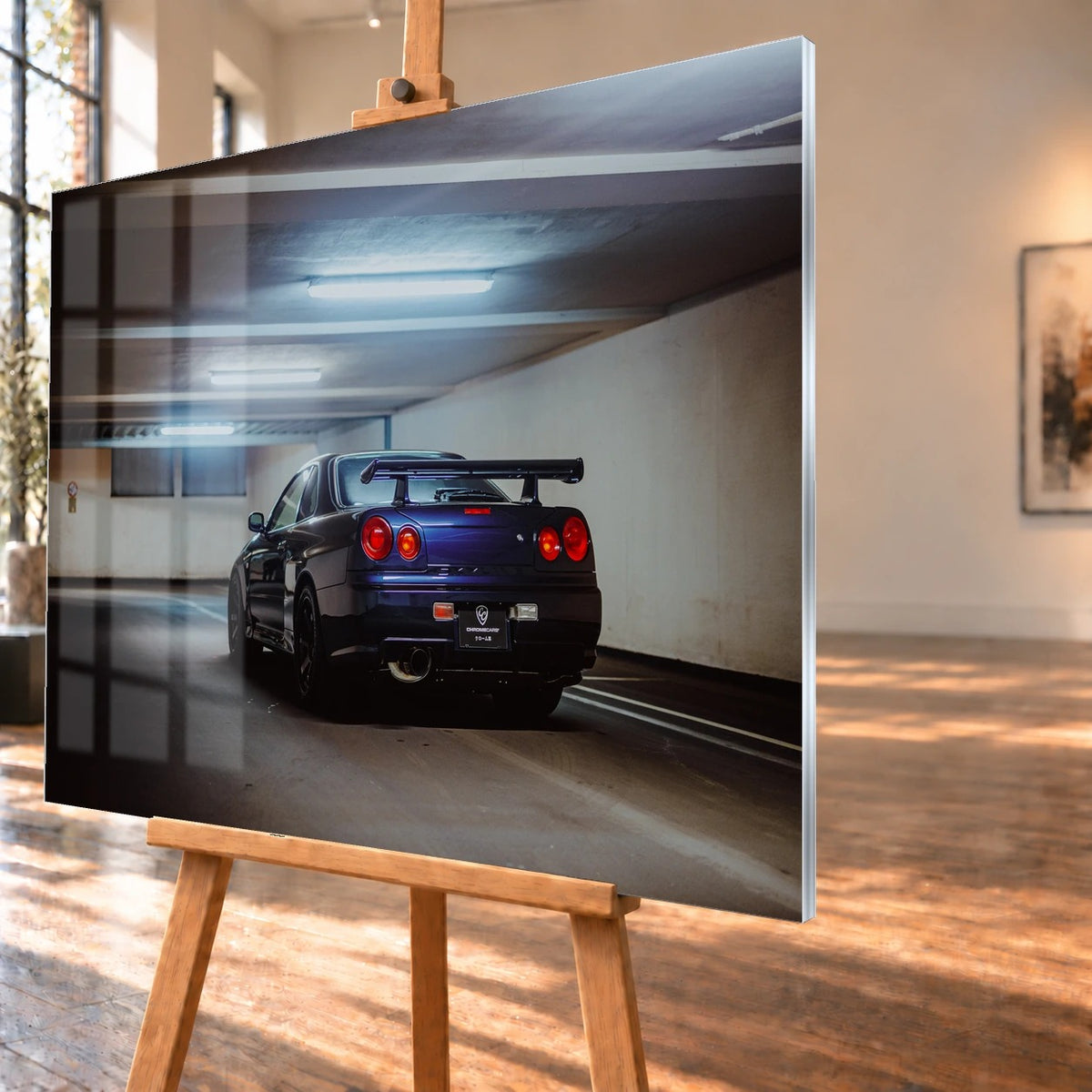 Der Nissan Skyline R34 steht schräg von hinten unter langen Deckenleuchten; Spoiler und rote Rundlichter führen die Perspektive. Motiv „Skyline Presence 2“ als Acrylglas-Wandbild, schräg von der Seite auf einer Holzstaffelei.