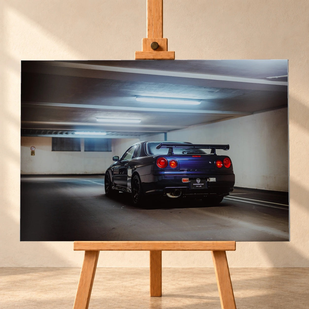 Der Nissan Skyline R34 steht schräg von hinten unter langen Deckenleuchten; Spoiler und rote Rundlichter führen die Perspektive. Motiv „Skyline Presence 2“ als Alu gebürstet-Wandbild, frontal auf einer Holzstaffelei.