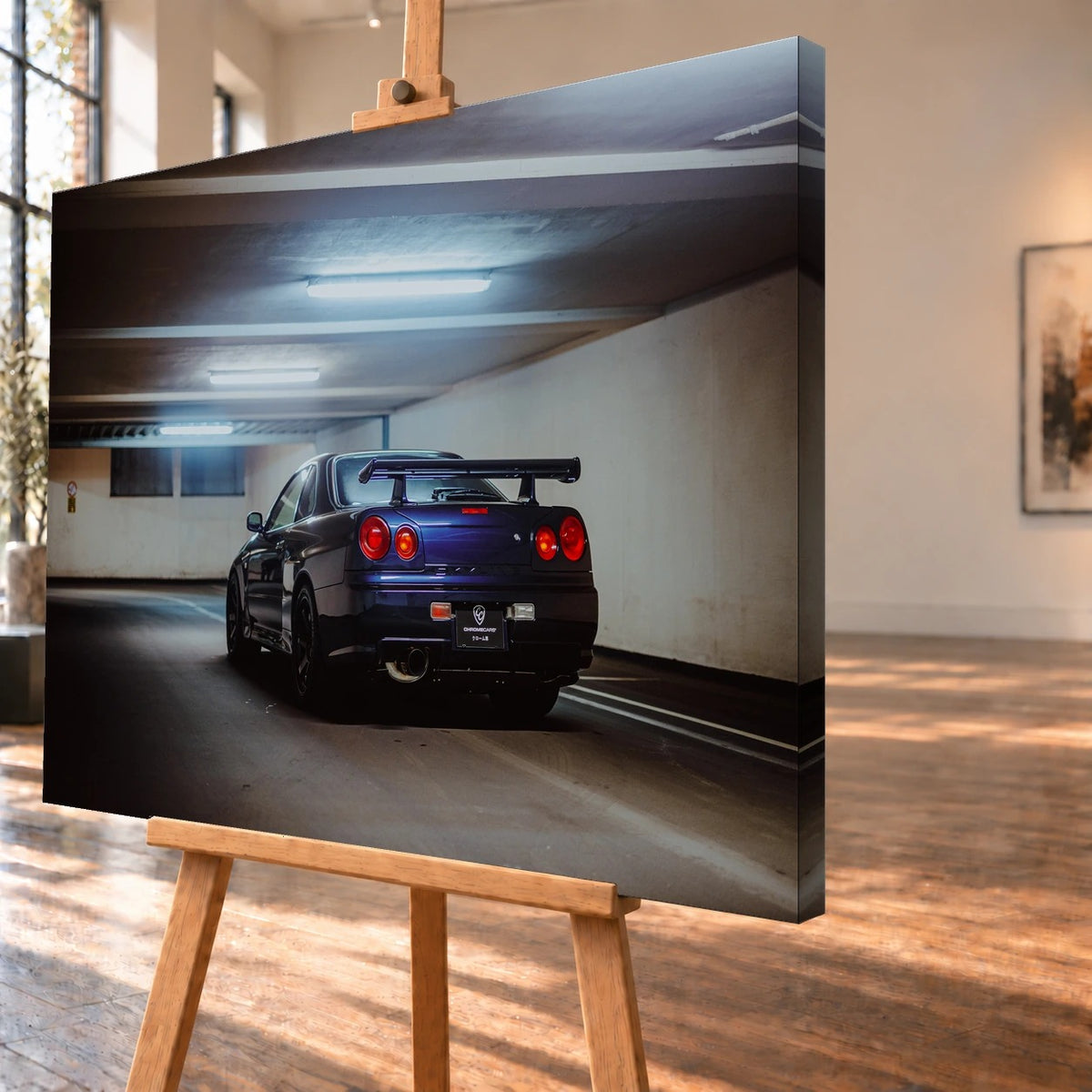 Der Nissan Skyline R34 steht schräg von hinten unter langen Deckenleuchten; Spoiler und rote Rundlichter führen die Perspektive. Motiv „Skyline Presence 2“ als Leinwand-Wandbild, schräg von der Seite auf einer Holzstaffelei.