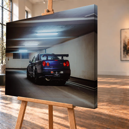 Der Nissan Skyline R34 steht schräg von hinten unter langen Deckenleuchten; Spoiler und rote Rundlichter führen die Perspektive. Motiv „Skyline Presence 2“ als Leinwand-Wandbild, schräg von der Seite auf einer Holzstaffelei.