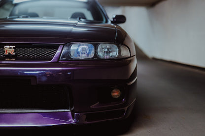 Die angeschnittene Front des Nissan Skyline R33 zeigt auf engem Raum Grill, Scheinwerfer und violetten Splitter als grafisches Detail. Originalmotiv „Urban Horizon“ im Querformat.