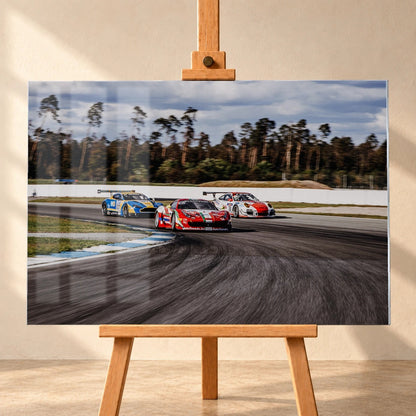 Aston Martin, Porsche und Ferrari GT3 fahren dicht gestaffelt durch eine Kurve; die Mehrwagen-Szene zeigt echtes Renngeschehen. Motiv „Racing Echo“ als Acrylglas-Wandbild, frontal auf einer Holzstaffelei.